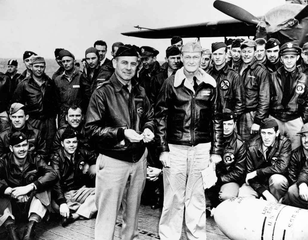 Lieutenant Colonel James H. Doolittle (left front), leader of the attacking force, and Captain Marc A. Mitscher, Commanding Officer of USS Hornet (CV-8), pose with a 500-pound bomb and USAAF aircrew members during ceremonies on Hornet's flight deck, while the raid task force was en route to the launching point. U.S. Naval History and Heritage Command Photograph.